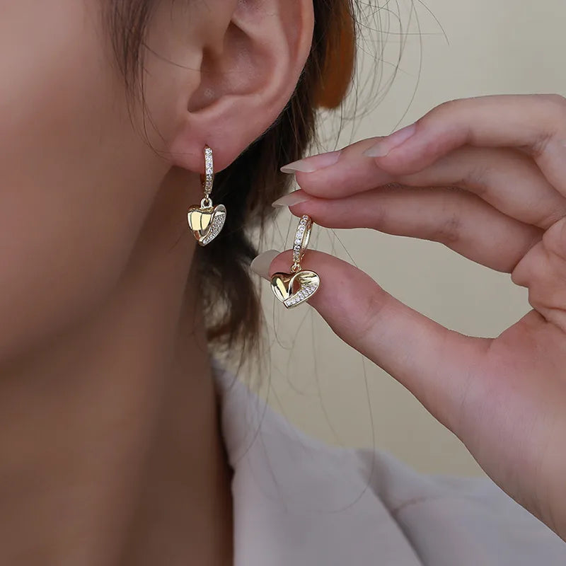 Boucles d’oreilles dorées en créoles, pendentif cœur pavé de zircons sur l’oreille
