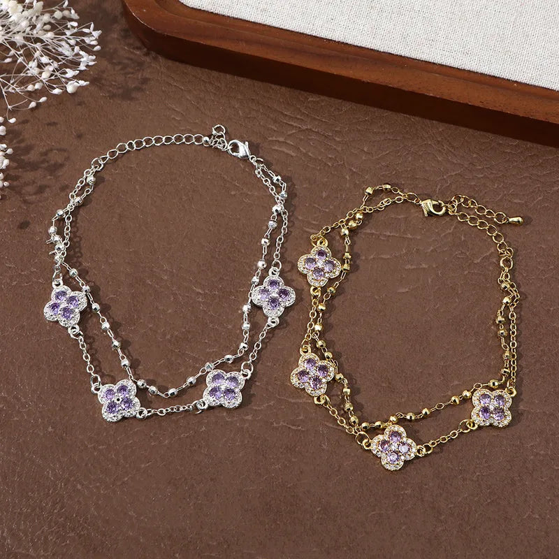 Deux bracelets double chaîne: argenté et doré, breloques trèfles zirconium violet.