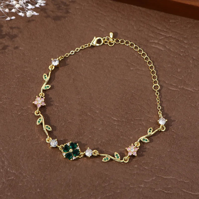 Bracelet double chaîne dorée, trèfle émeraude central, feuilles vertes et fleurs rose