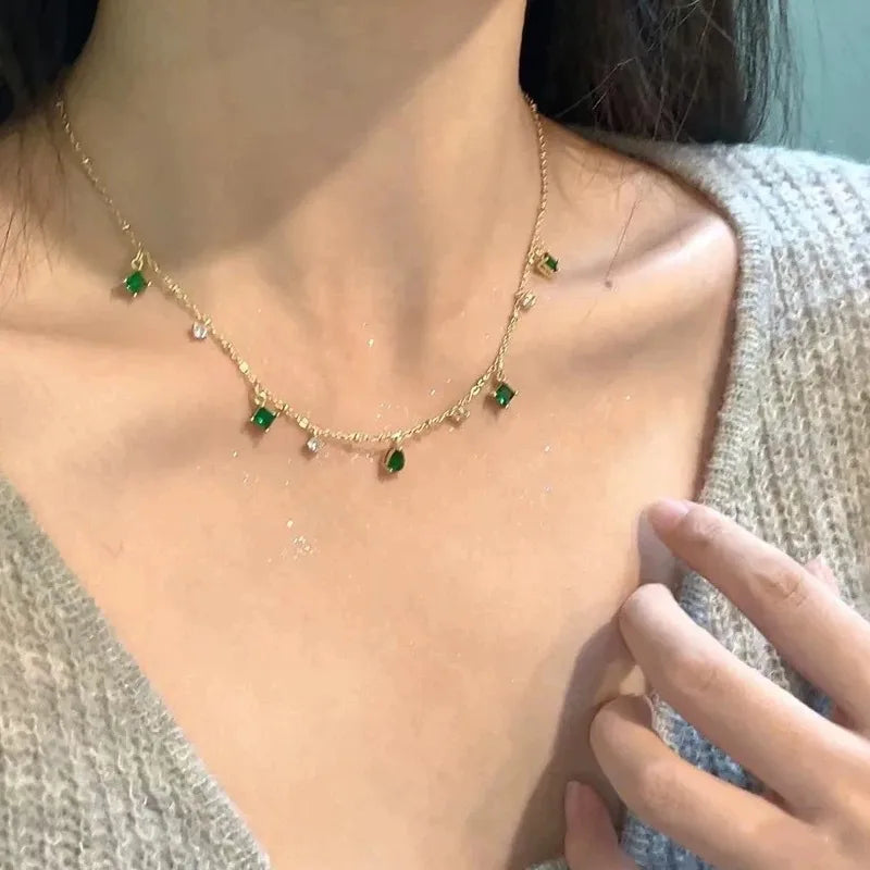 Collier fin à chaîne dorée, pierres vertes émeraude et petits zircons blancs, porté.