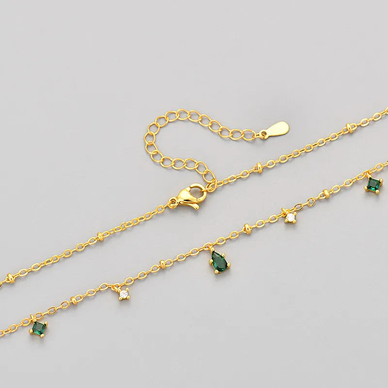 Détails du collier : chaîne dorée avec pierres vertes émeraude et zircons blancs.
