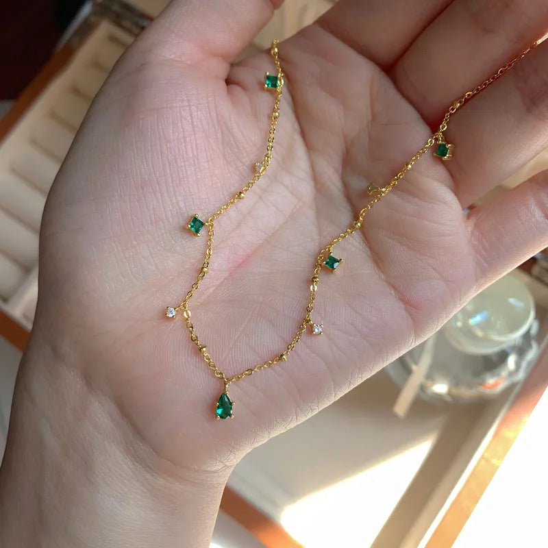 Collier à chaîne dorée en vue rapprochée, pierres vertes émeraude et zircons blancs.