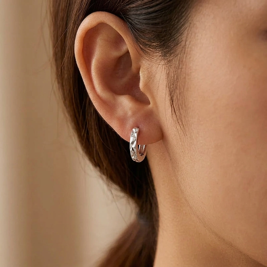 Créoles argentées effet diamanté portées, anneau fin à facettes géométriques.