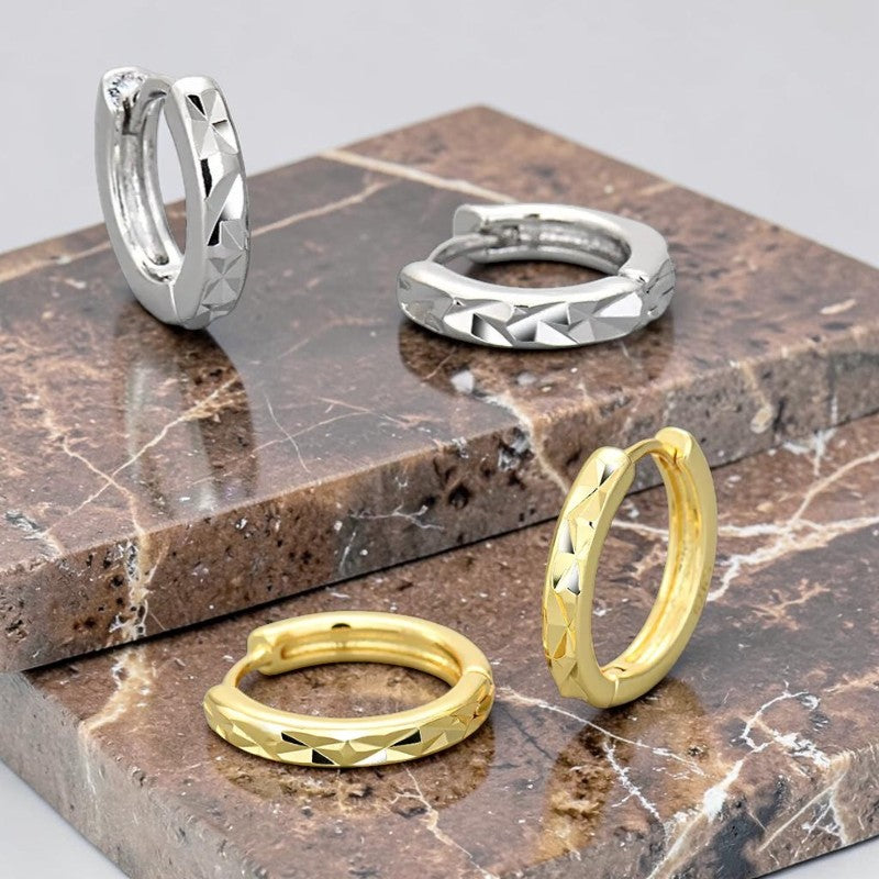 Créoles argentées effet diamanté portées, anneau fin à facettes géométriques.