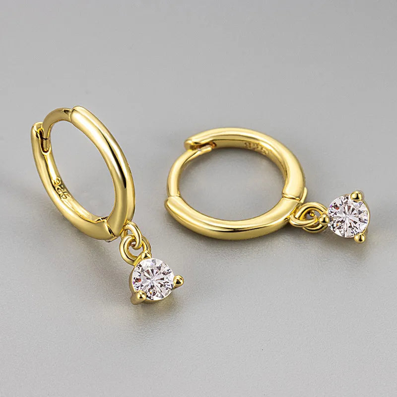 Créoles pendantes dorées, anneaux ovales avec zircon solitaire blanc.