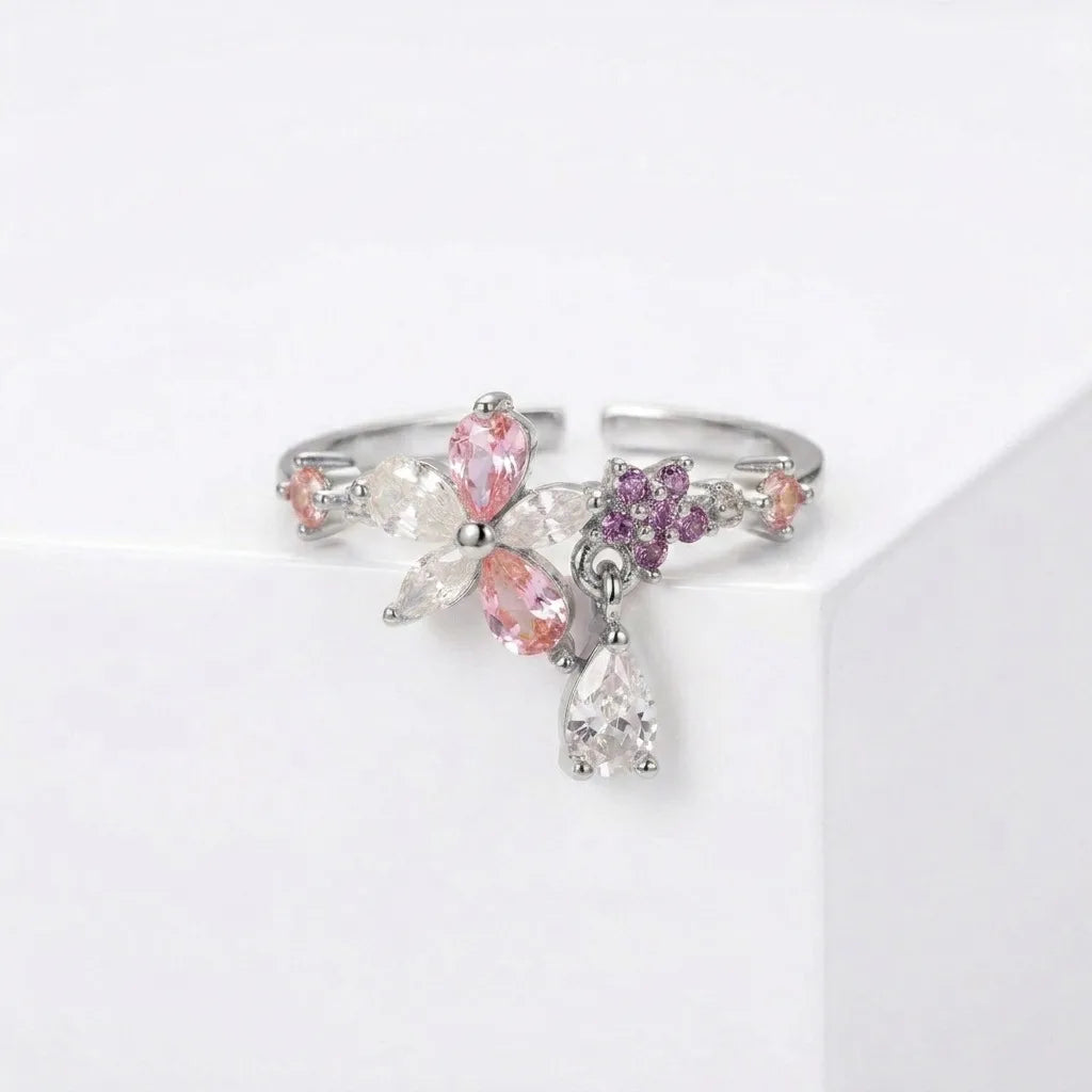 Bague ajustable argentée en acier inoxydable avec motif floral, zircons roses et violets et pampille goutte sur fond blanc