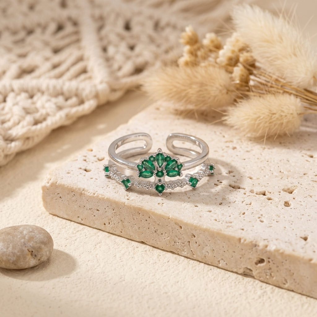 Bague ajustable argentée à motif floral avec zircons verts posée sur un décor beige