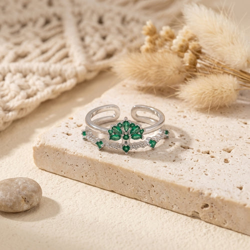 Bague ajustable argentée à motif floral avec zircons verts posée sur un décor beige
