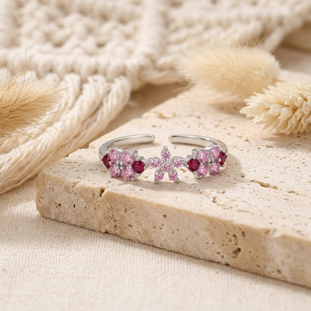 Bague ajustable argentée avec bouquet floral de zircons roses et fuchsia posée sur une pierre claire