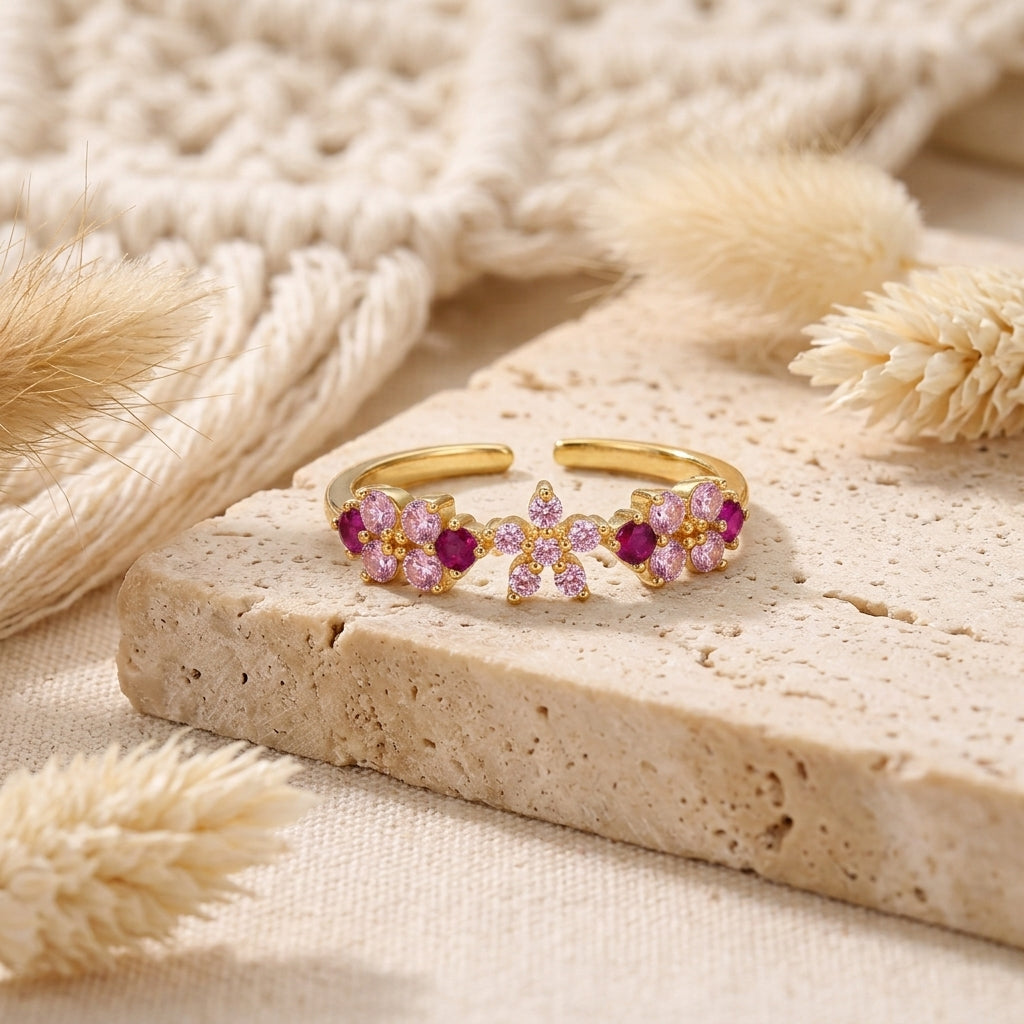 Bague ajustable dorée avec bouquet floral de zircons roses et fuchsia posée sur une pierre claire