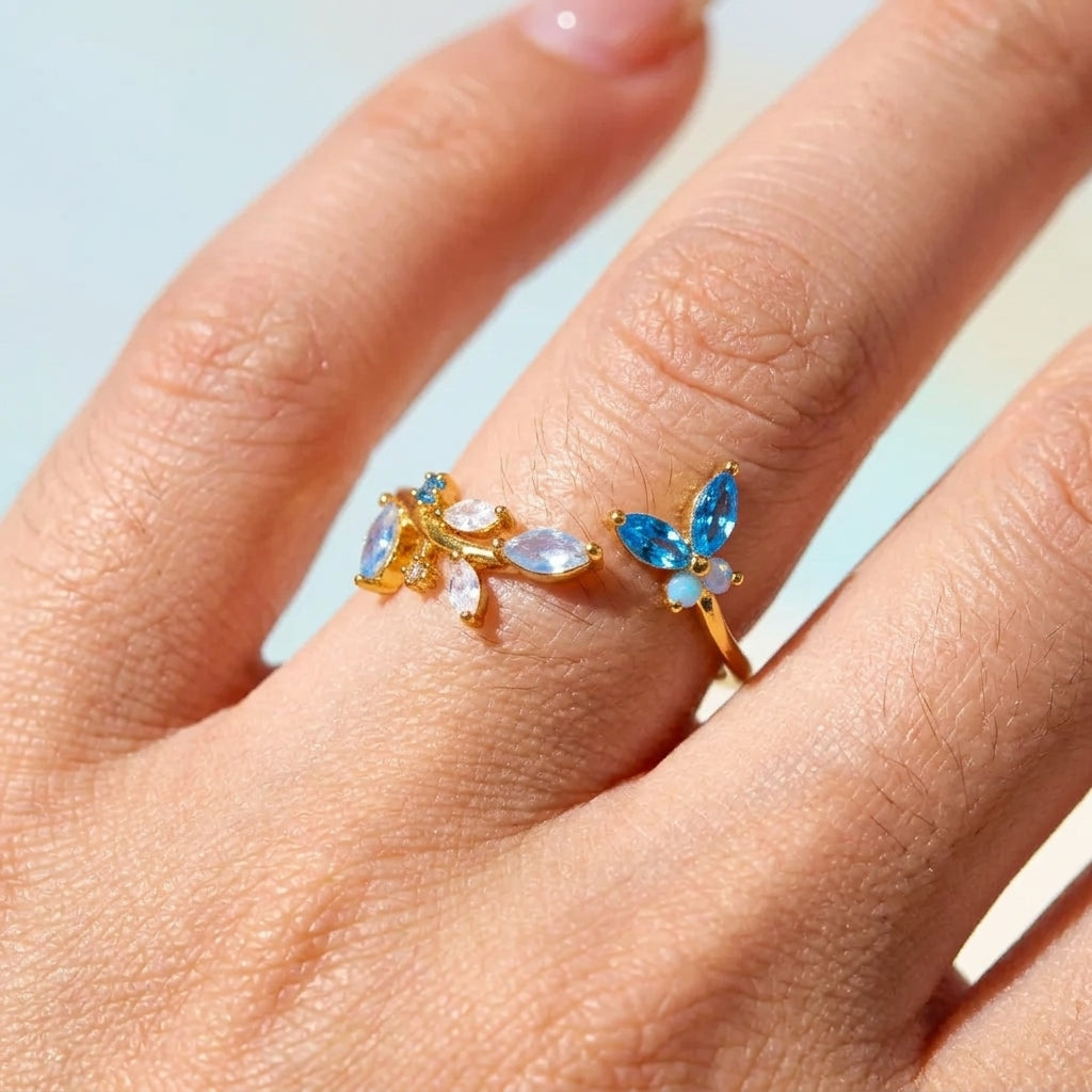 Bague ajustable dorée portée au doigt, papillon azur en zircons bleus marquises et fleurs opalines blanches, style féerique – Jewelry by Kitana