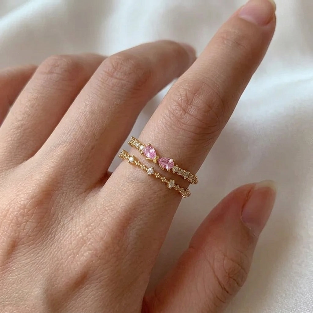 Bague double rang nœud zircon rose pastel ajustable plaquée or 18K portée à la main, deux anneaux fins pavés de cristaux et nœud poire rose central — Jewelry by Kitana
