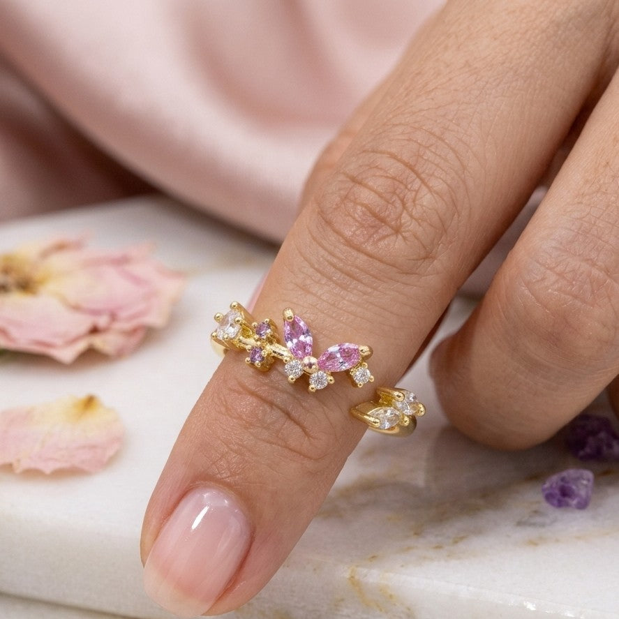 Bague papillon dorée plaquée or portée, pierres roses et cristaux blancs sur l’annulaire