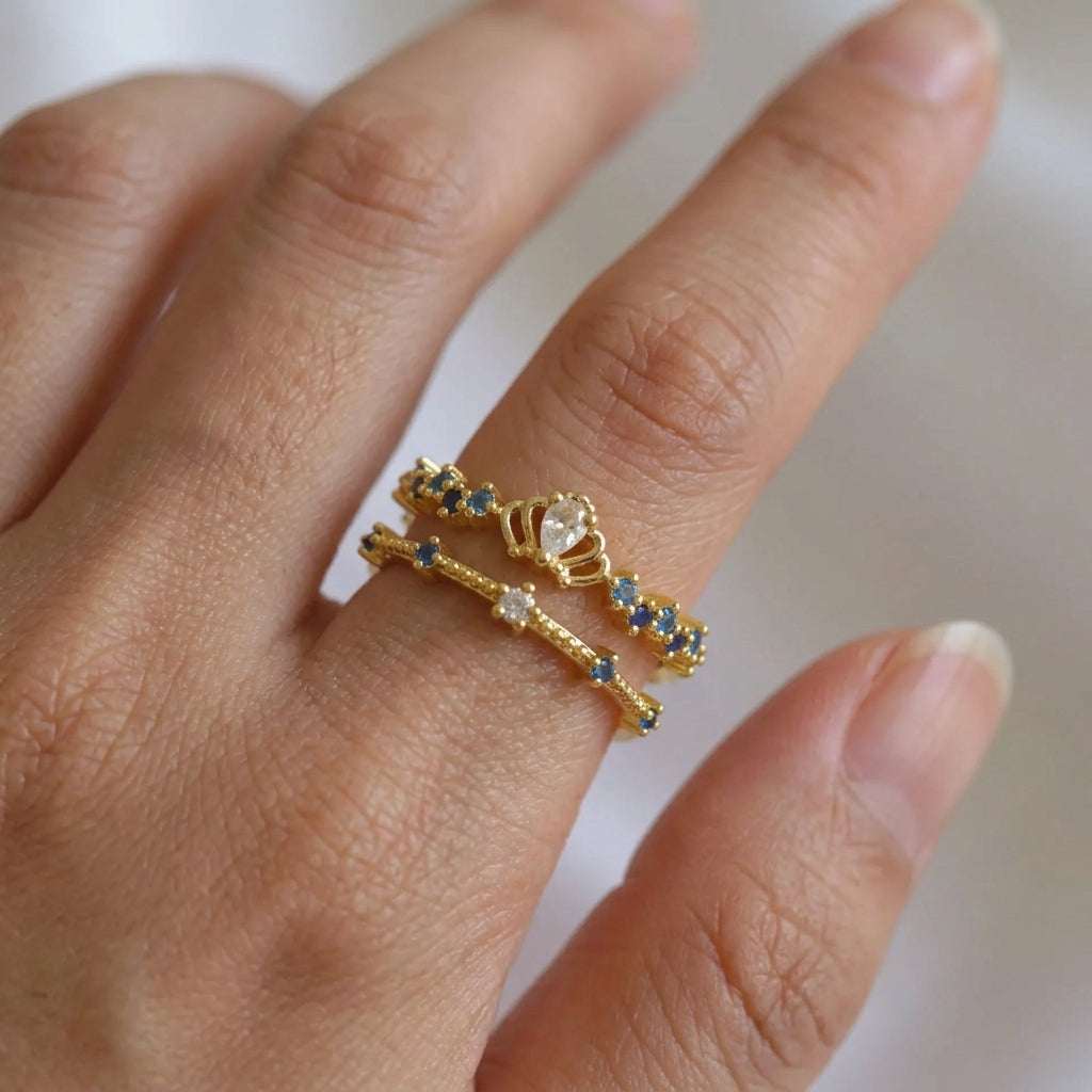 Bague double rang dorée portée au doigt, couronne avec cristal central et zircons bleus saphir, ajustable – Jewelry by Kitana