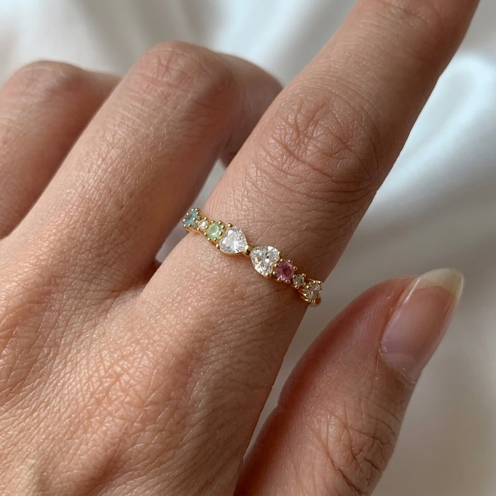 Bague dorée portée au doigt, rang de zircons multicolores pastel avec pierres centrales blanches en cœur, style éternité – Jewelry by Kitana