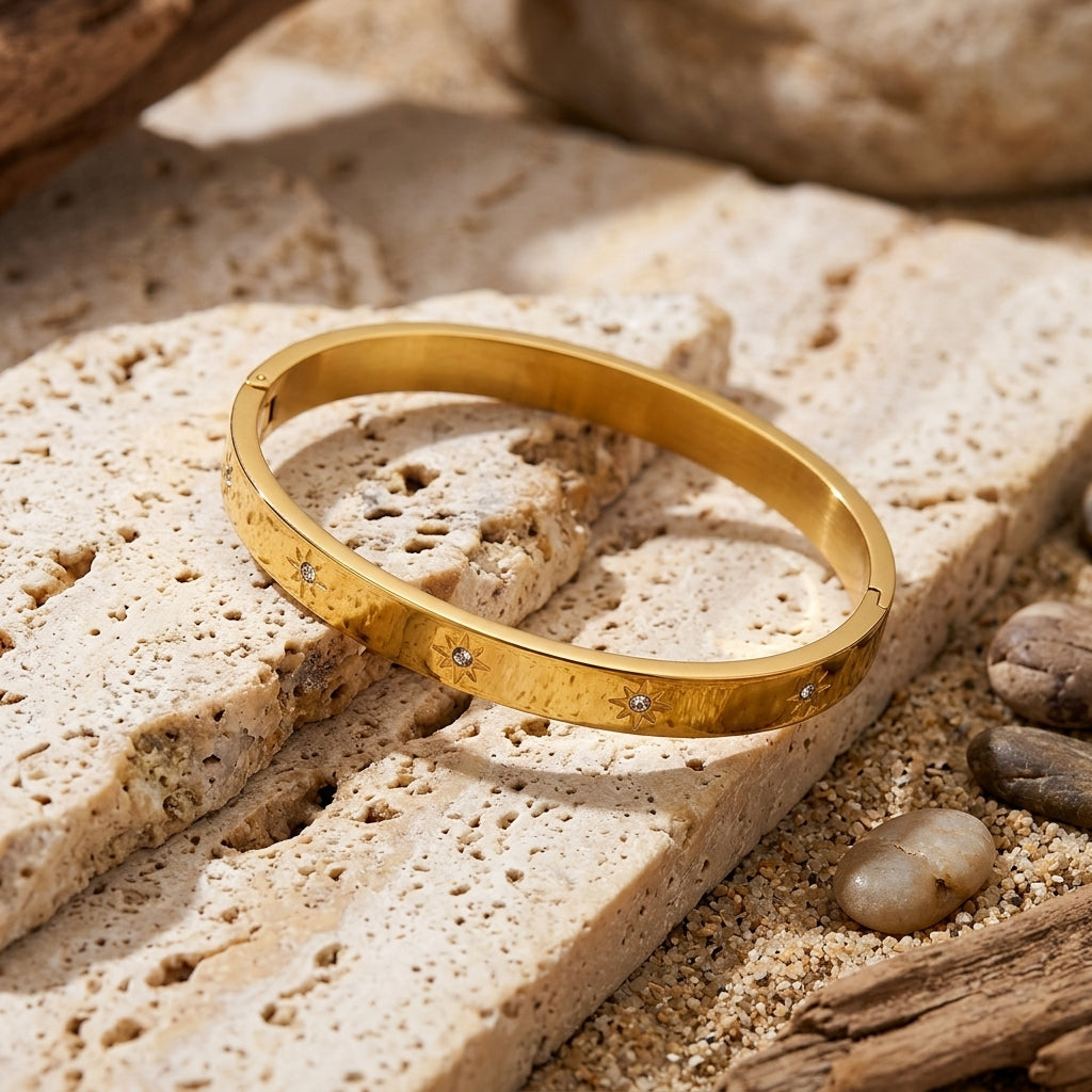 Bracelet jonc doré avec étoiles et zircons posé sur une pierre claire