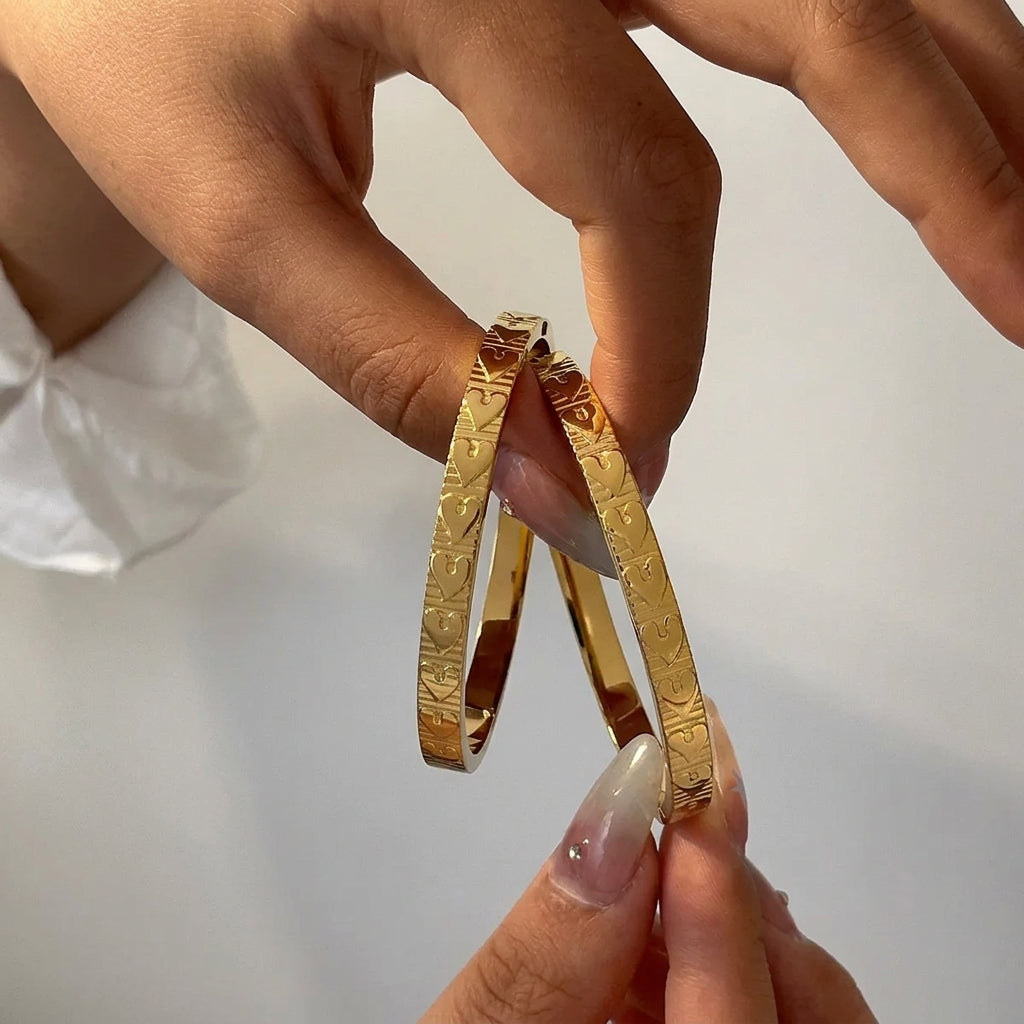 Bracelet jonc doré avec motif cœur en relief tenu entre les doigts
