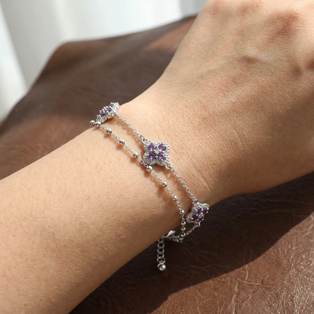 Bracelet double chaîne argenté porté au poignet, motifs trèfle porte-bonheur en zircons violet améthyste, chaîne fine avec perles et extension réglable