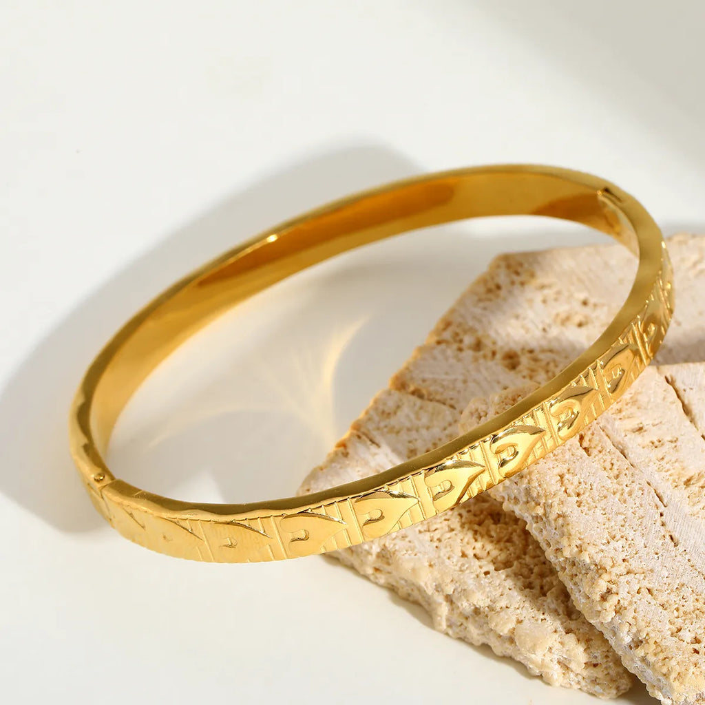 Bracelet jonc doré à motif cœur en relief posé sur un tissu clair