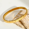 Bracelet jonc doré à motif cœur en relief posé sur un tissu clair