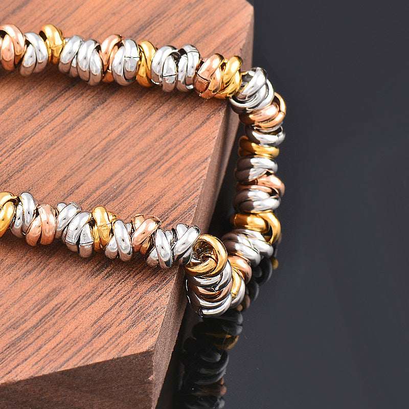 Bracelet souple tricolore en acier inoxydable doré, argenté et rose doré présenté sur un support en bois
