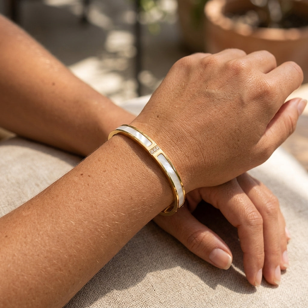 Bracelet jonc nacré doré avec strass porté au poignet 
