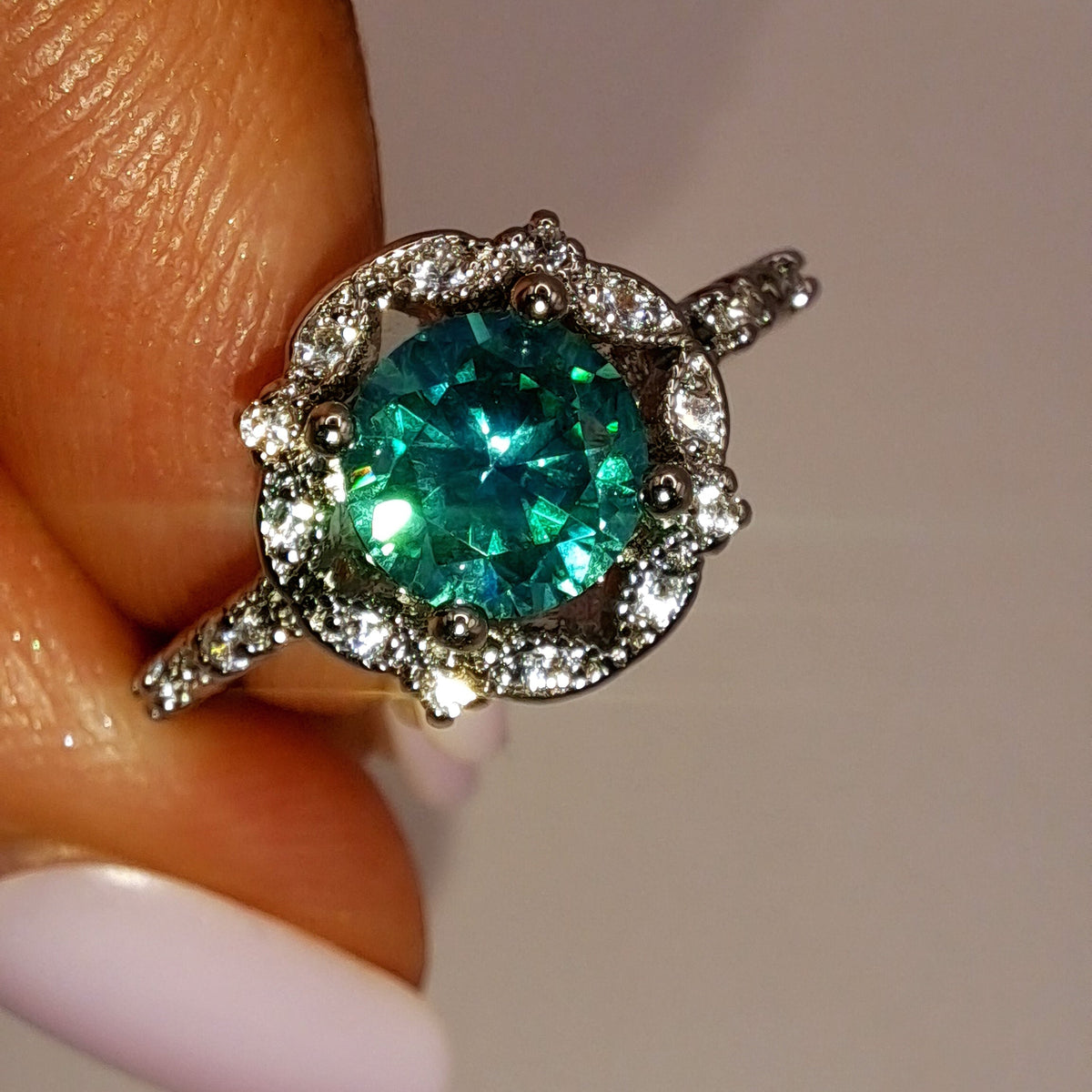 Gros plan réel de la bague avec zircon vert d’eau et halo de zircons blancs
jewelry by kitana 